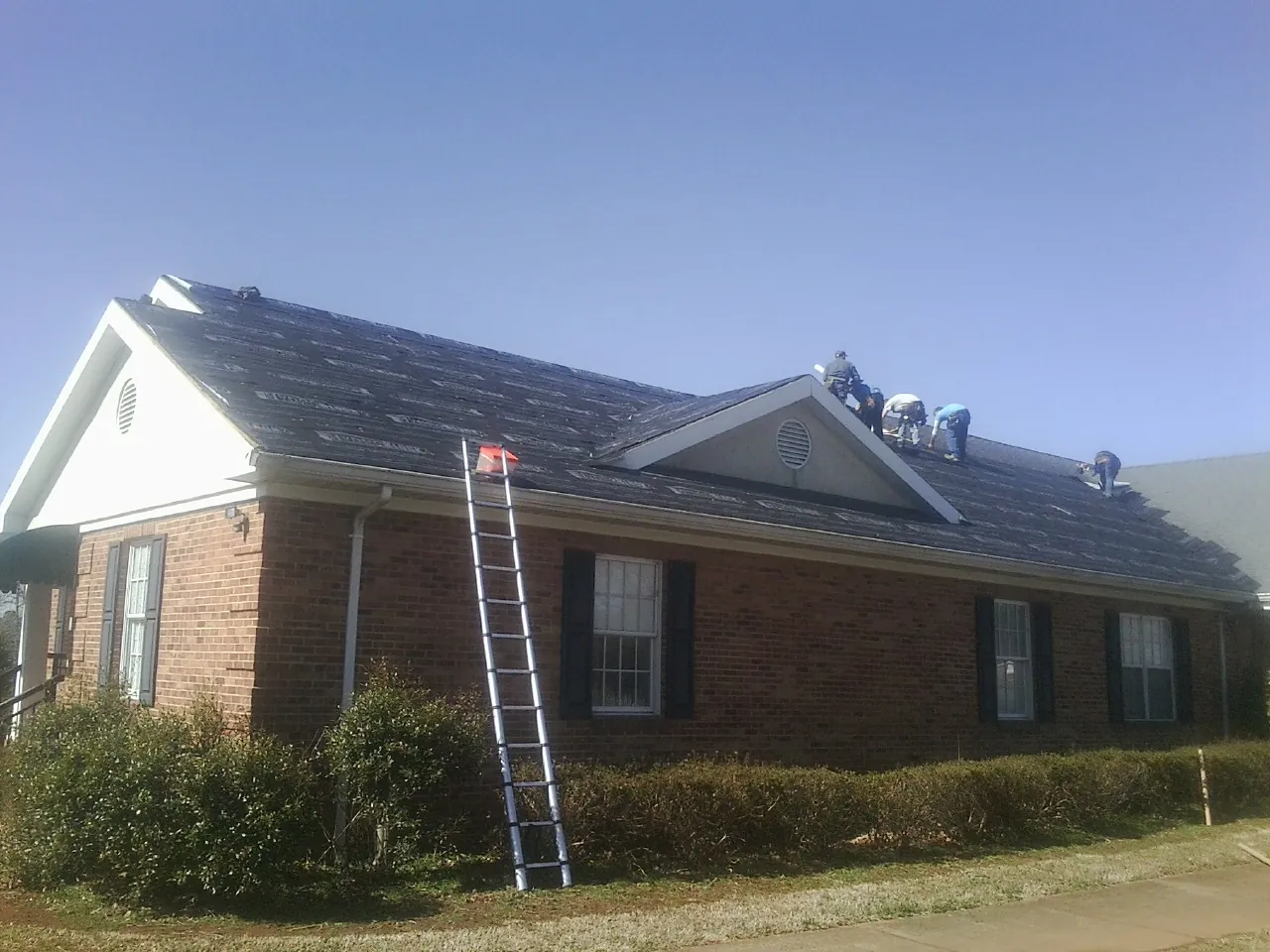 Crew tearing shingles off a brick ranch roof with a ladder set — Metal Roof Repair work by our crew in Hartford City