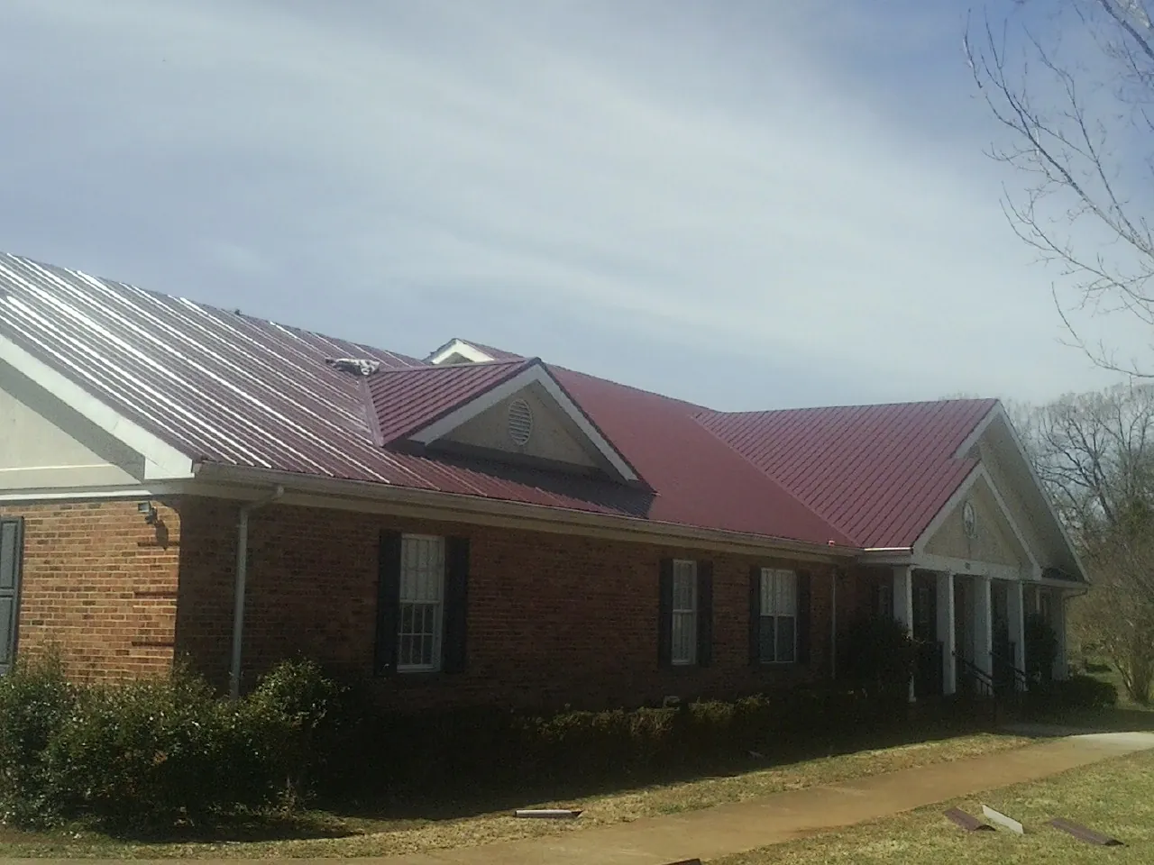 Red metal roof with gabled entries on a long brick building, from a Hail Damage Roof Repair job in Hartford City
