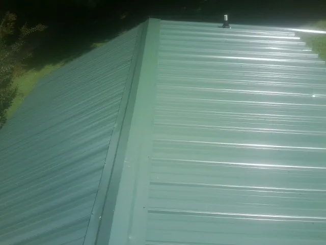 New green metal panels meeting at the ridge of a roof — Flat Roof Repair work by our crew in Hartford City
