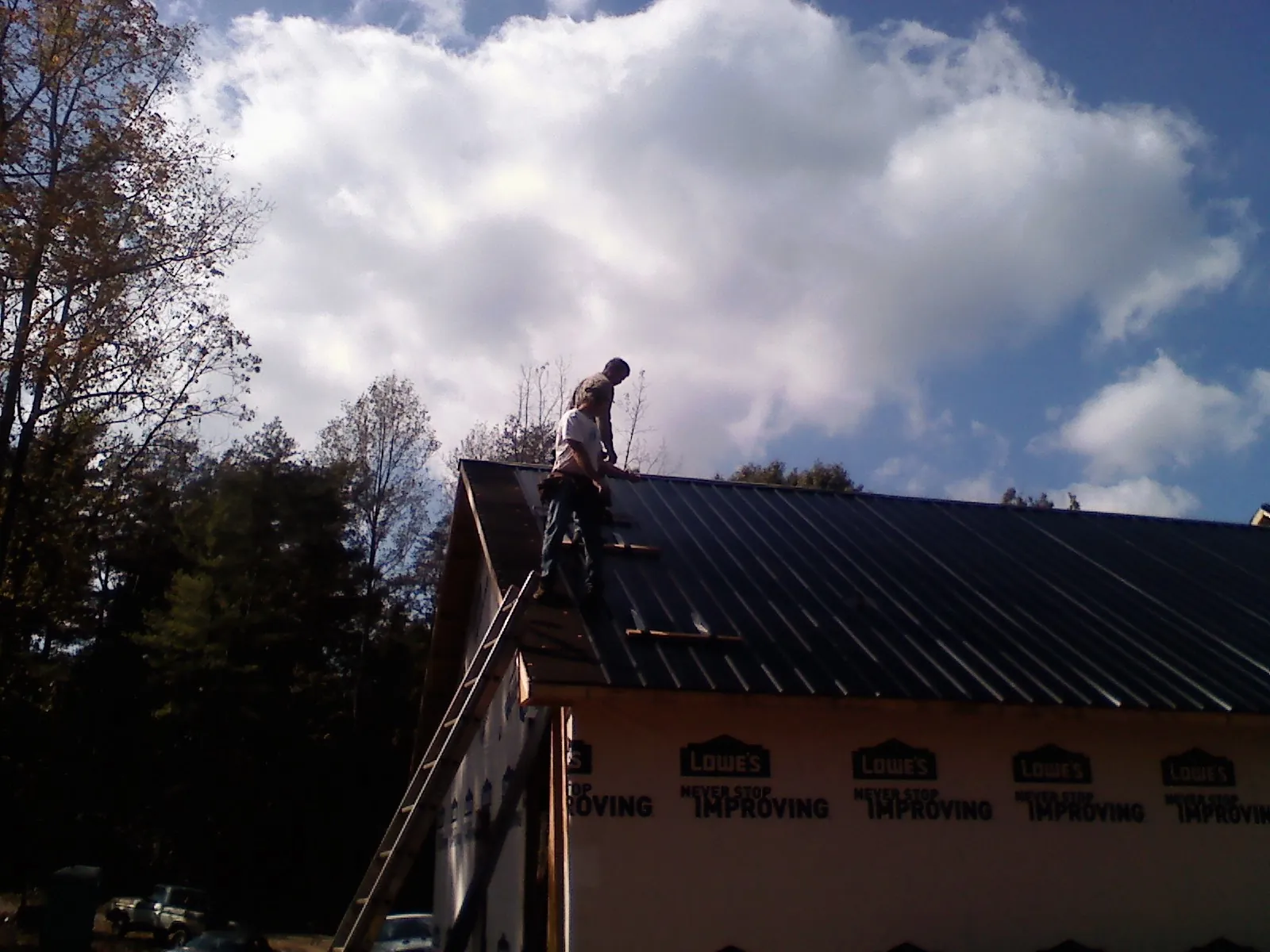 Roofer fastening dark metal panels high against a cloudy sky, from a Roof Inspection job in Hartford City