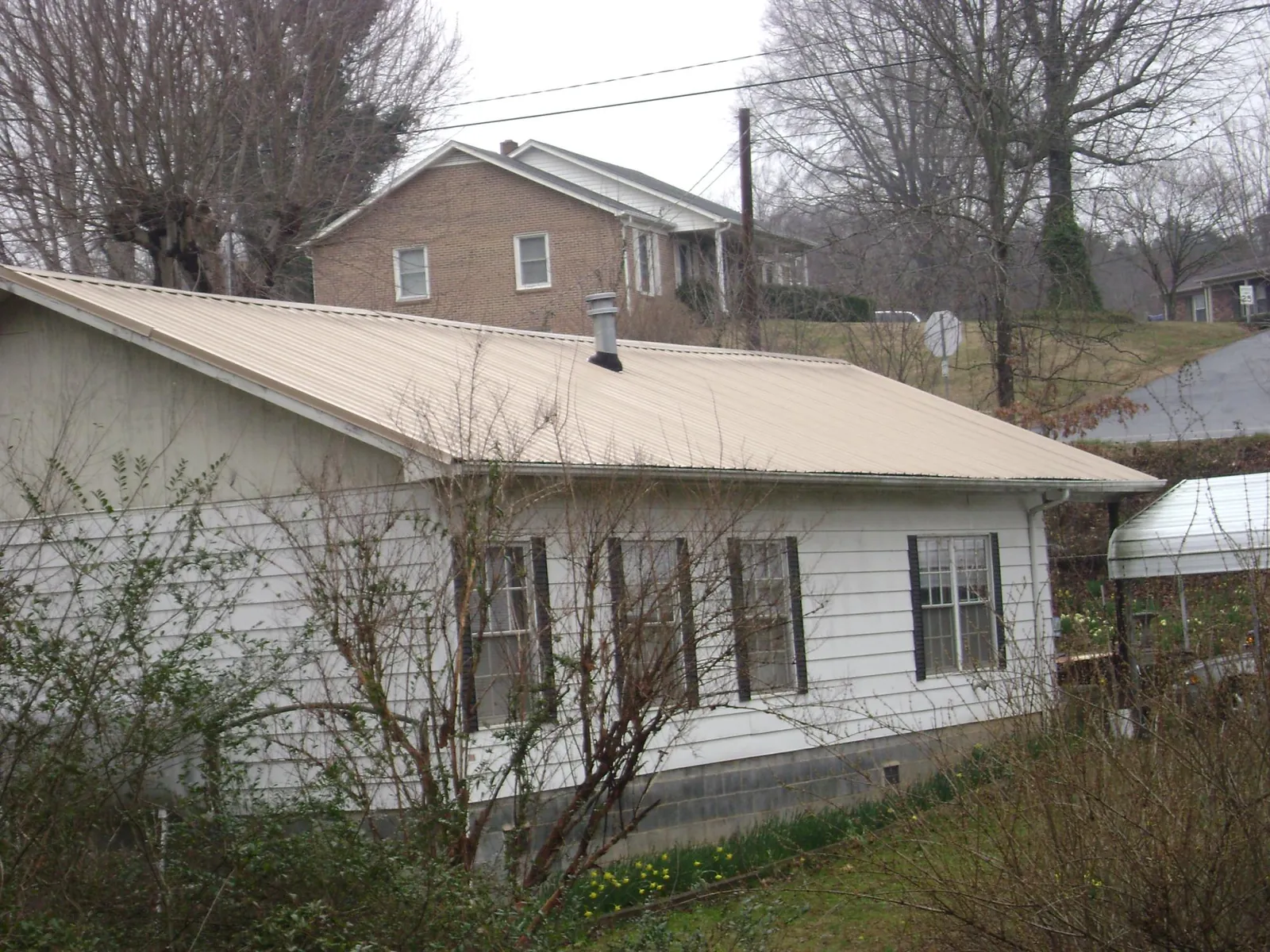 Tan metal roof on a white sided house set into a hillside — Commercial Roofing by Roofing Brothers in Hartford City