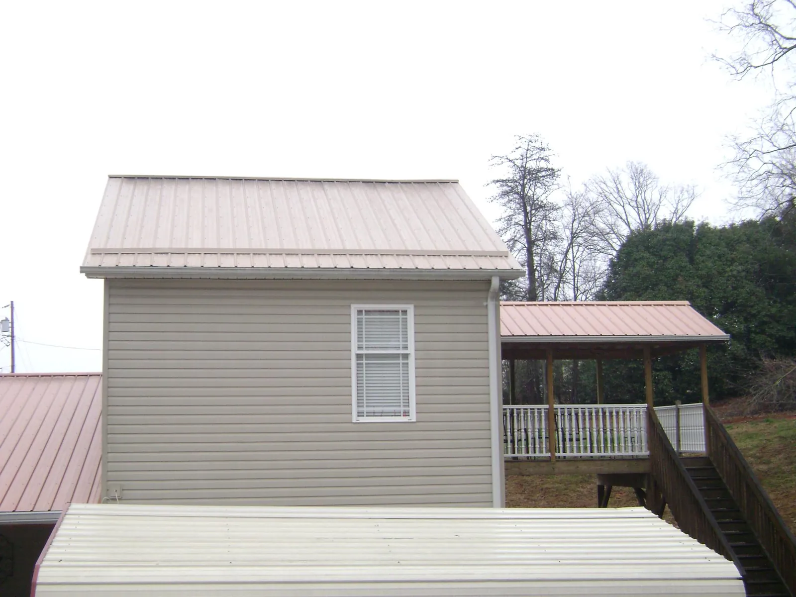 Tan metal roofs on a two story addition and attached porch, from a Roof Replacement job in Hartford City
